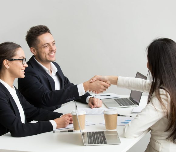 Friendly satisfied partners handshaking at group meeting thanking for successful teamwork, smiling millennial businessman shaking hand greeting businesswoman, respect or making contract deal concept